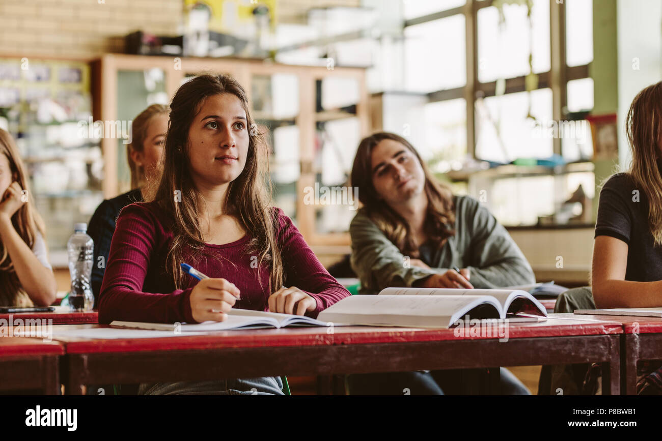 Beautiful young woman sitting in class with classmates around paying attention to the lecture. Young people studying at the high school. Stock Photo