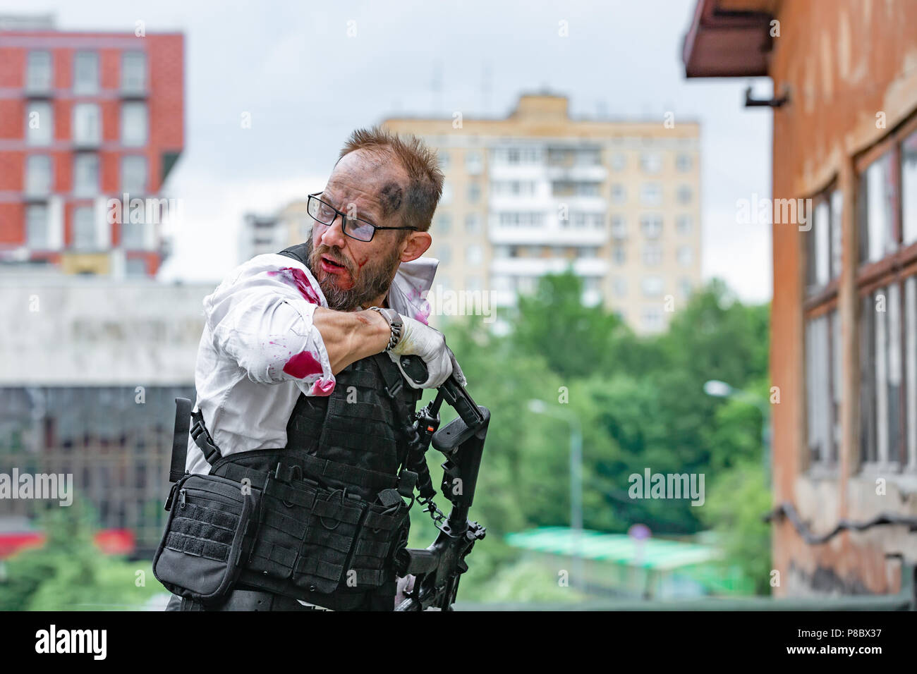 man dressed in a bulletproof vest, a shirt in his blood, pursues a victim with a gun Action