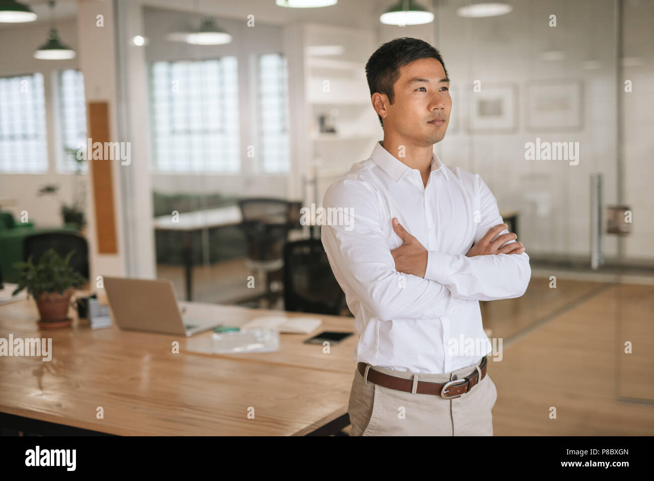 Focused Asian businessman standing in an office deep in thought Stock Photo