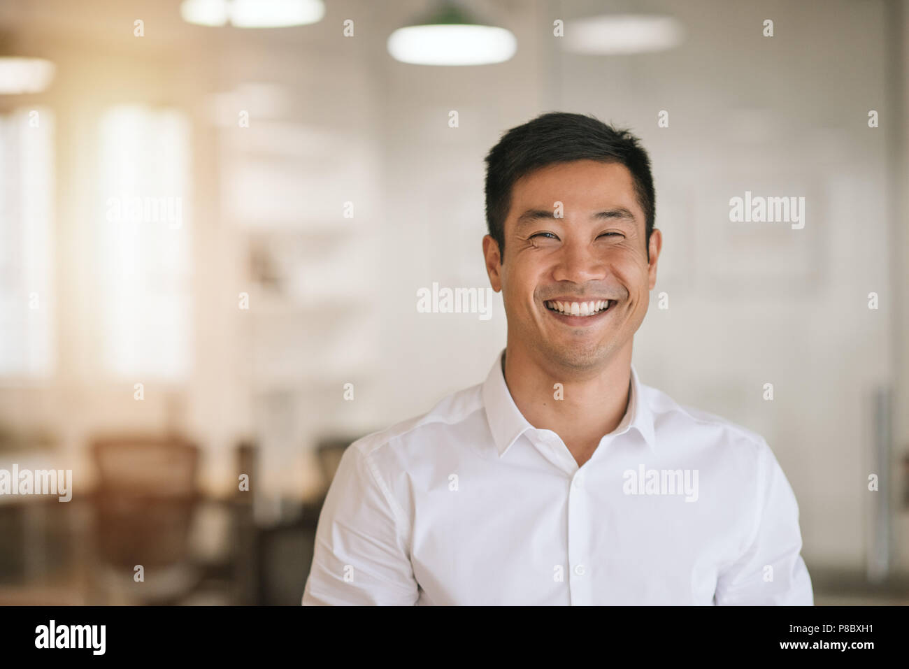 Smiling Asian businessman standing in a bright modern office Stock Photo