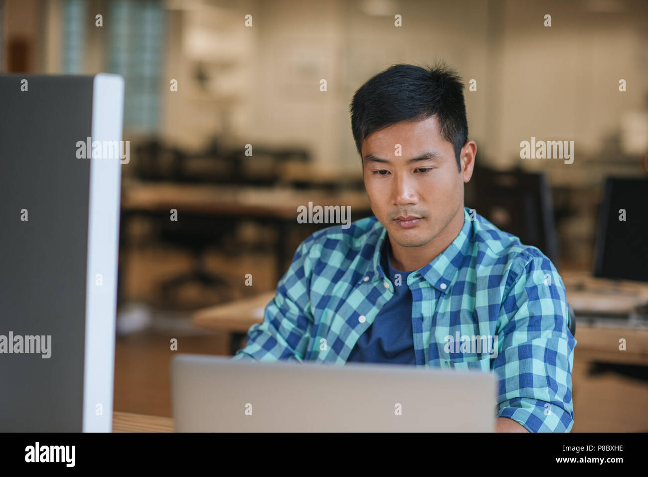Focused young Asian designer using a laptop at his desk Stock Photo