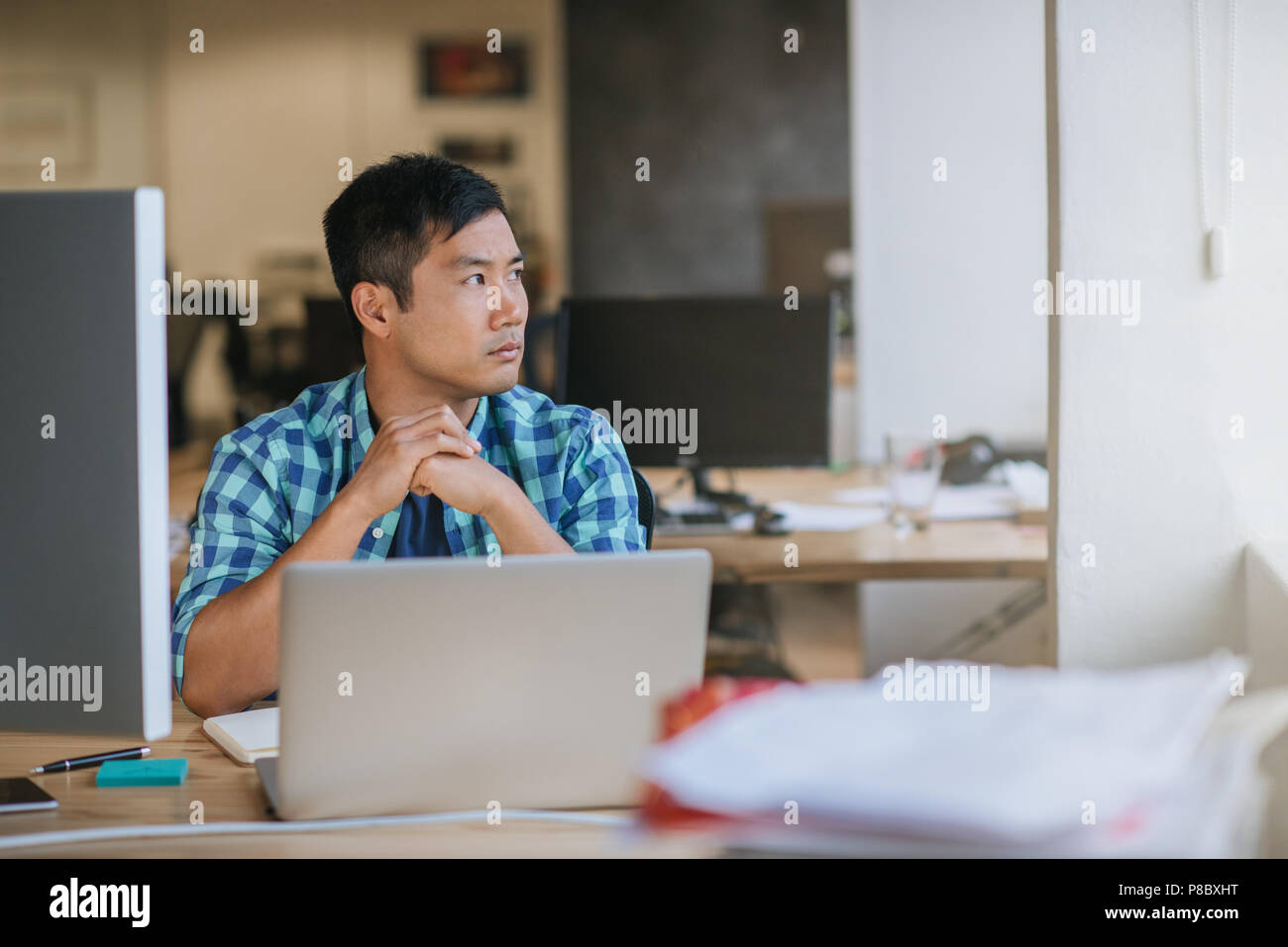 Asian designer sitting at his desk deep in thought Stock Photo