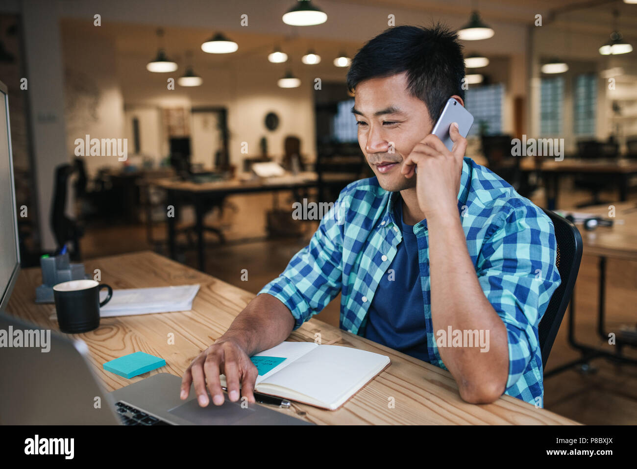 Smiling Asian designer talking on a cellphone and working online Stock Photo
