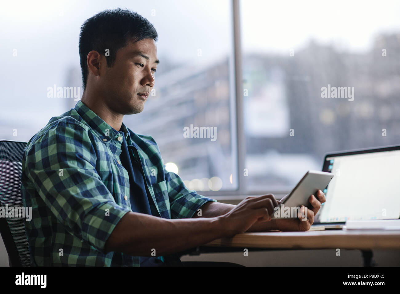 Young Asian designer using a tablet at his office workstation Stock Photo