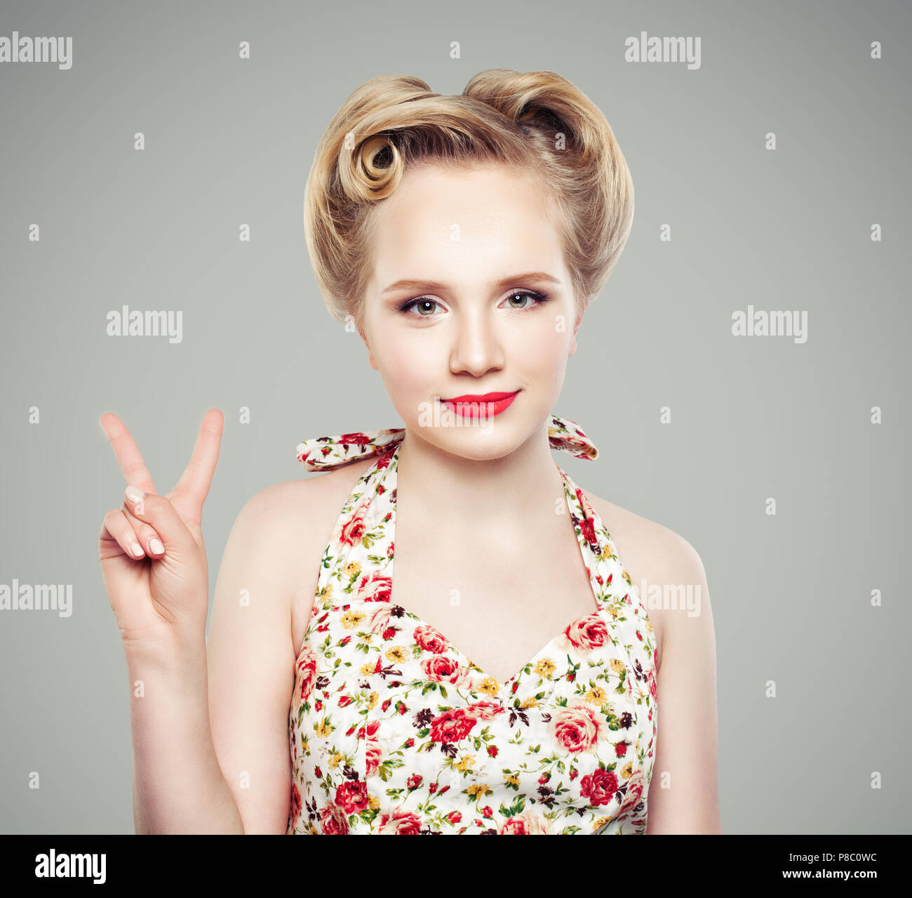 Beautiful retro vintage pin-up girl showing two fingers. Victory hand sing or peace gesture. Young blonde woman with makeup and perfect hairstyle Stock Photo