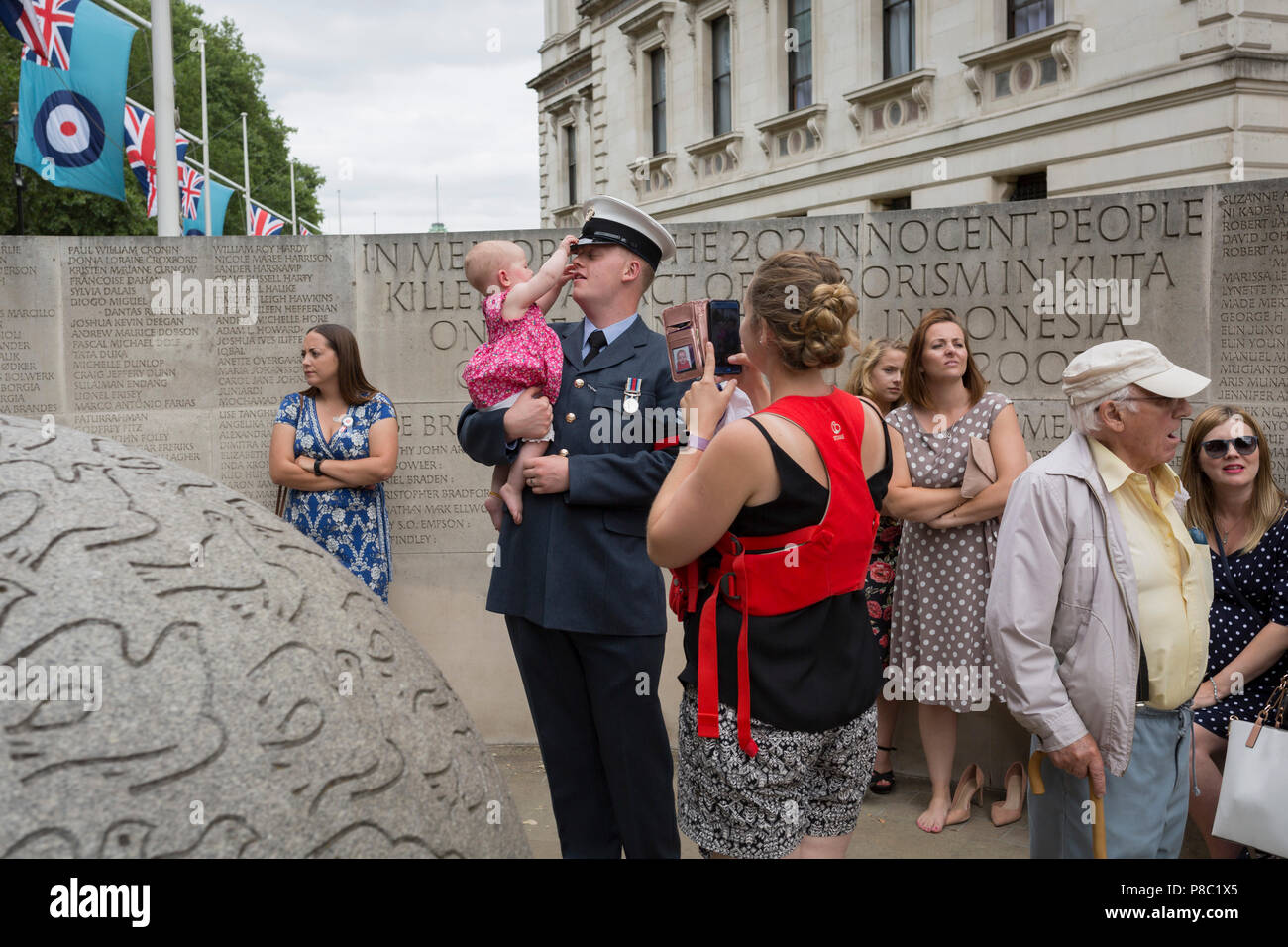 On the 100th anniversary of the Royal Air Force (RAF) and following a flypast of 100 aircraft formations representing Britain's air defence history which flew over central London, a serviceman holds his child next to the memorial to those killed in the 2002 Bali bombing, on 10th July 2018, in London, England. Stock Photo