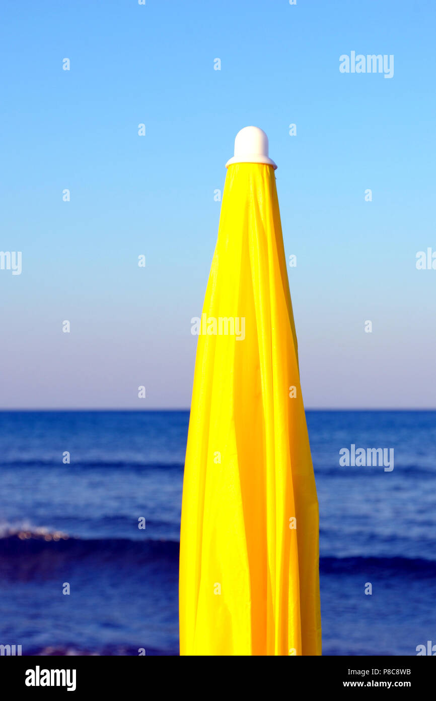 closed yellow parasol on the beach early morning, with waves sea and blue sky on background Stock Photo