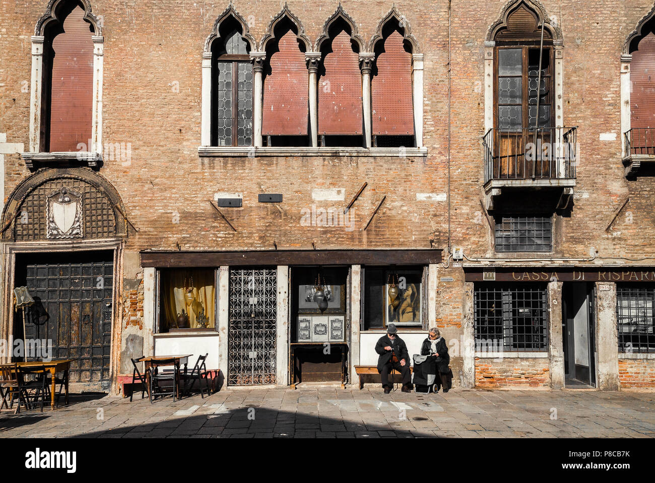 Elderly man and woman sitting in front of old Venetian building in bright spring sunlight, Venice Italy Stock Photo