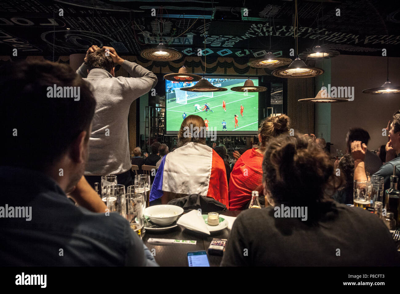 Picture of a group of French supporters in a restaurant watching on a giant screen the semi final match France belgium, during the 2018 FIFA World Cup,, which saw the victory of French team. The 2018 FIFA World Cup is the 21st FIFA World Cup, an international football tournament contested by the men's national teams of the member associations of FIFA once every four years. It is currently ongoing in Russia starting from 14 June and will end with the final match on 15 July 2018 Stock Photo