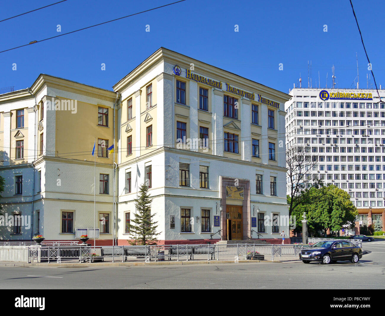 The building of the university on a city street with flagpoles standing next to it with fluttering flags and passing by the car on the road. . For you Stock Photo