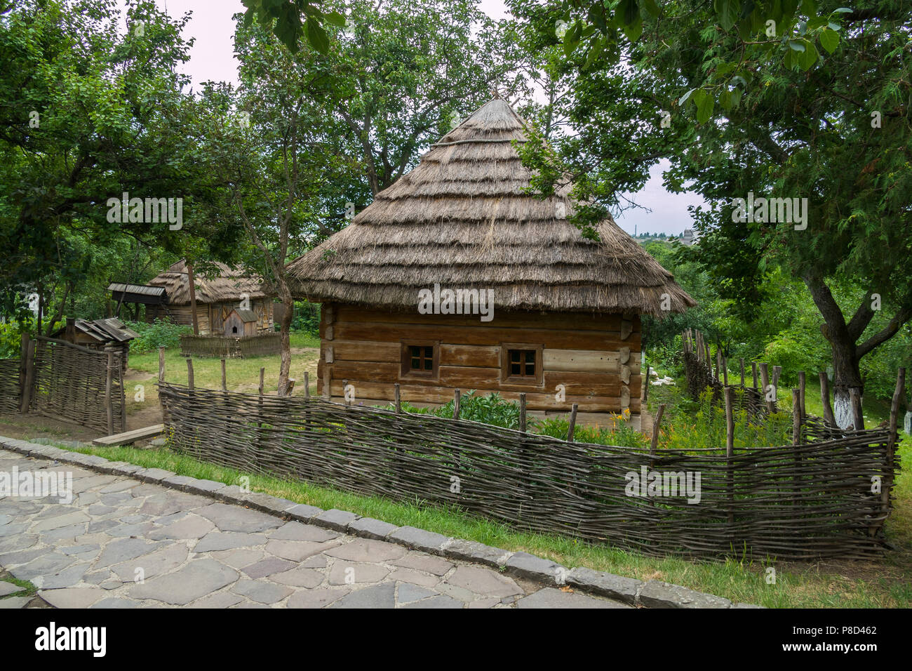 A rural house under a thatched roof with small windows in the wall behind a wattle fence in a picturesque area in the shade of a tree. . For your desi Stock Photo