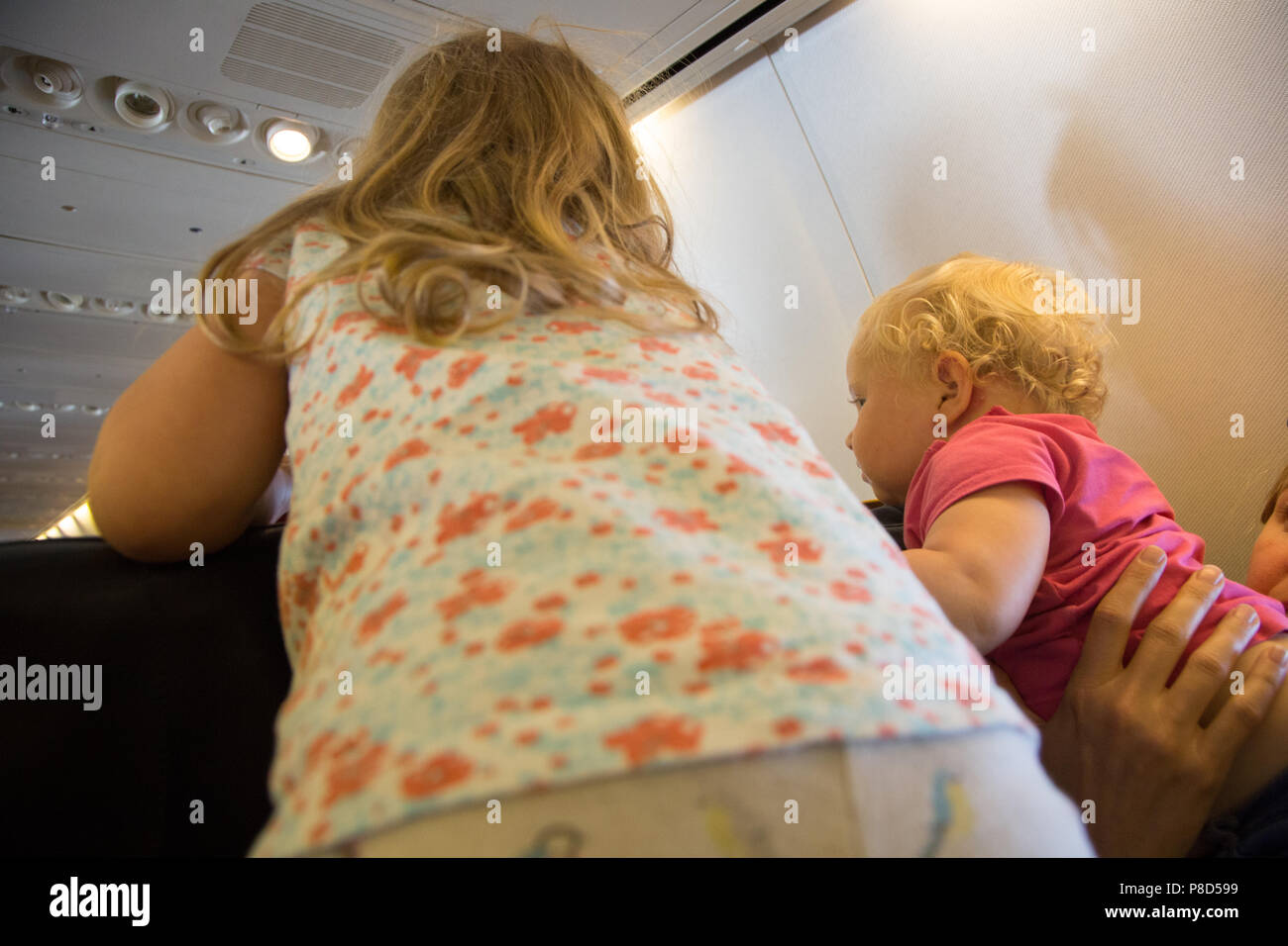Young girls on an aeroplane seat look at the passengers sitting behind Stock Photo