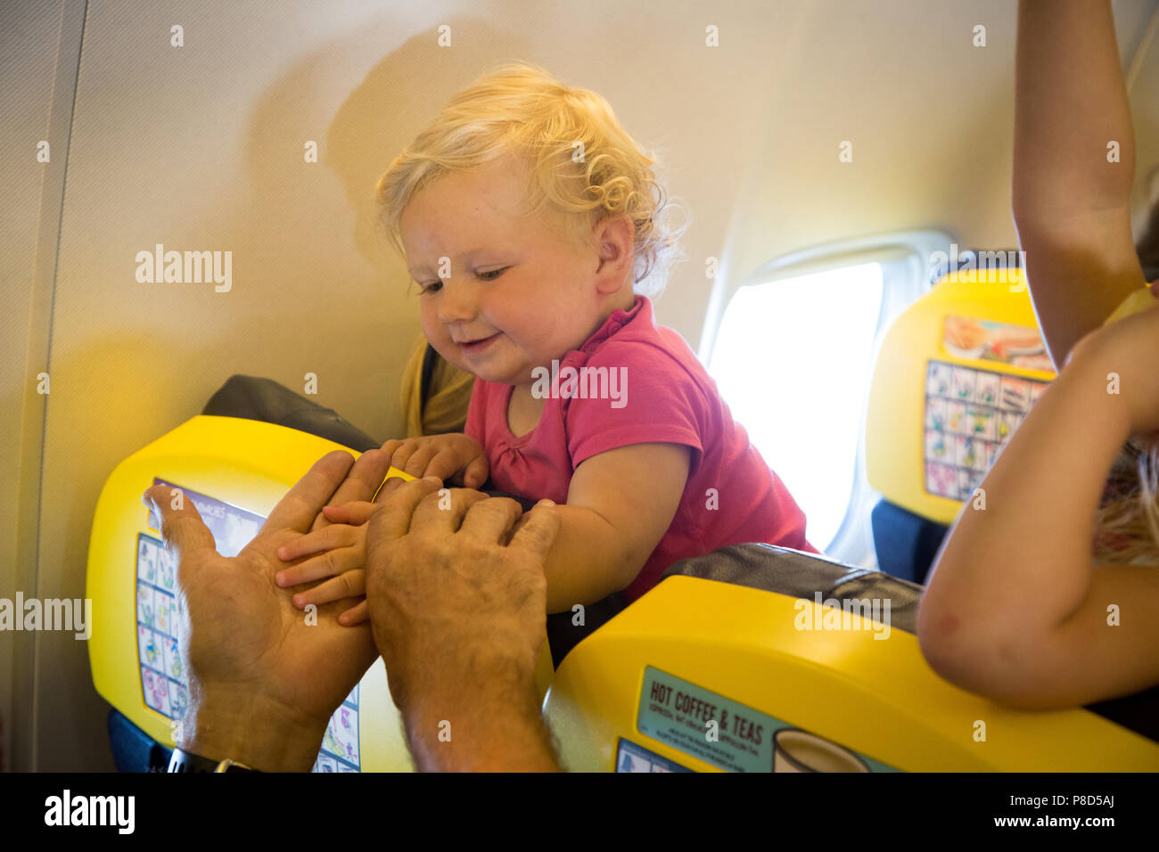 Young girls on an aeroplane seat look at the passengers sitting behind Stock Photo