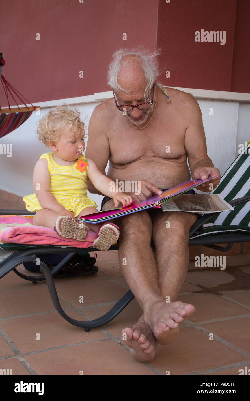 A grandfather reads a book with his infant one year old granddaughter Stock Photo