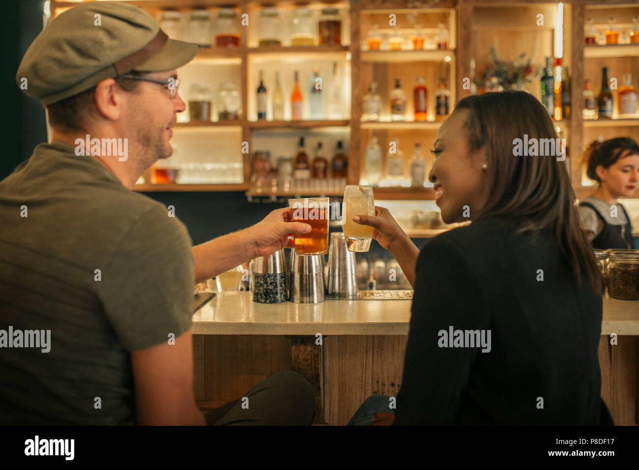Two smiling friends sitting in a bar cheering with drinks Stock Photo