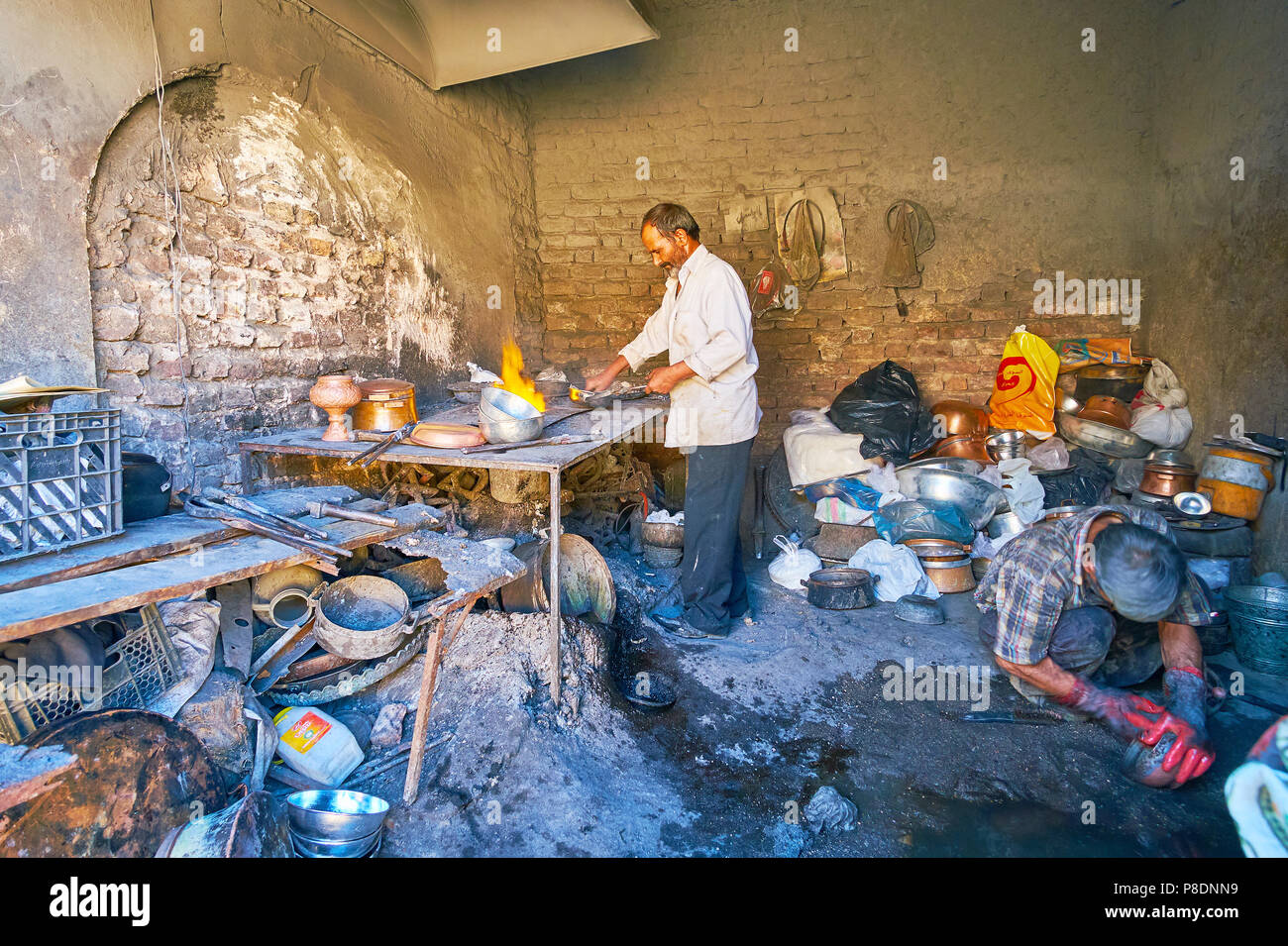 KERMAN, IRAN - OCTOBER 15, 2017: The workshop of cookware cleaners, that use fire, sand and small stones to clean, re-season and restore the old pans, Stock Photo