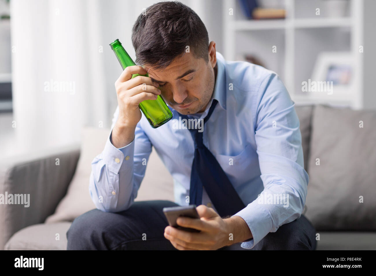alcoholic with smartphone drinking beer at home Stock Photo