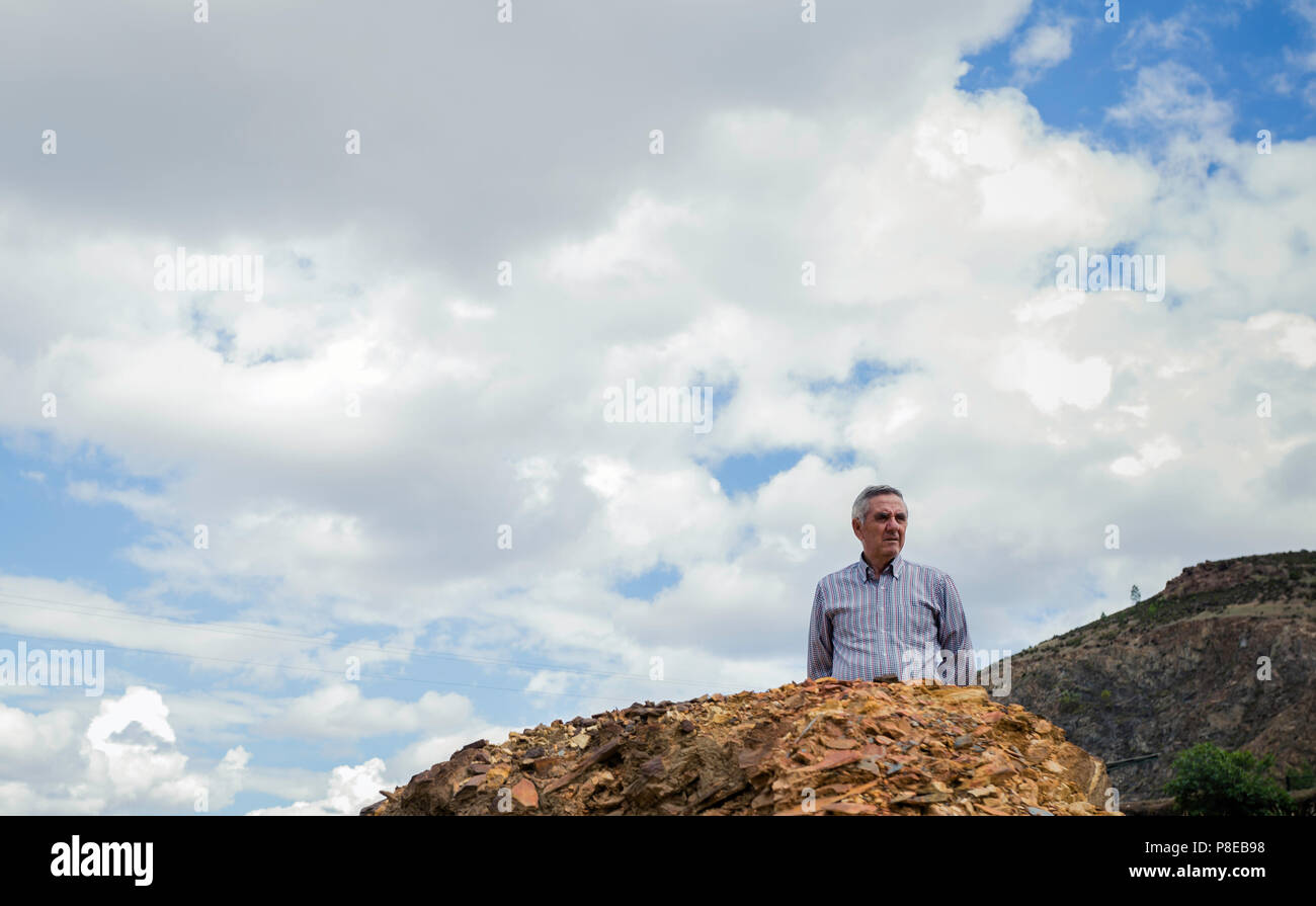 Elderly man standing looking at the landscape behind rocks, looking half body with the sky with clouds in the background at the Zaranda mines, Spain Stock Photo