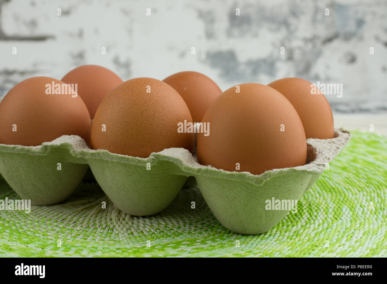 CLOSE UP OF CARTON OF SIX BROWN RANGE HEN EGGS ON URBAN BACKGROUND AND GREEN MAT Stock Photo