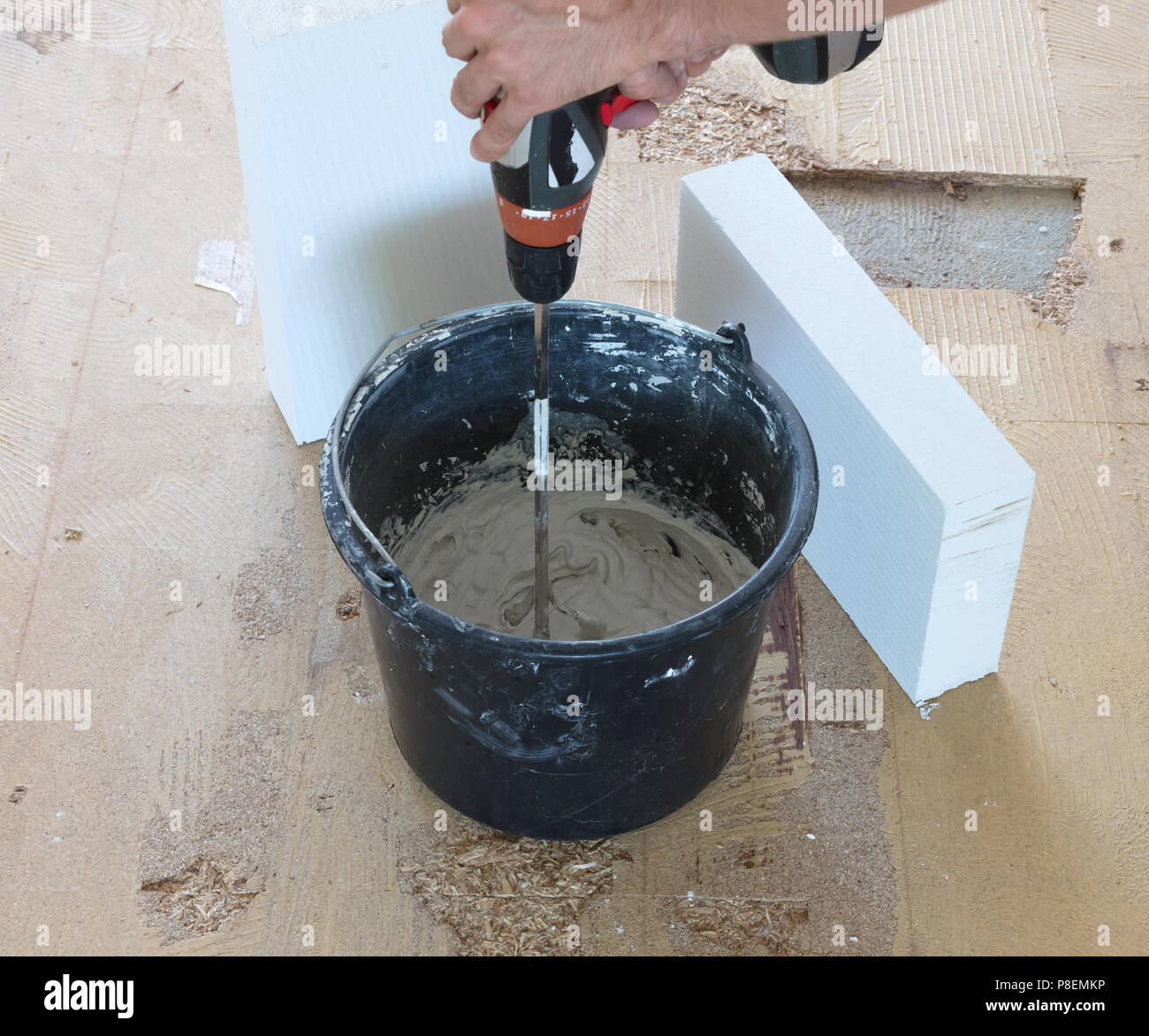 Man is holding drill mixer in his hands. Man is mixing grey concrete
