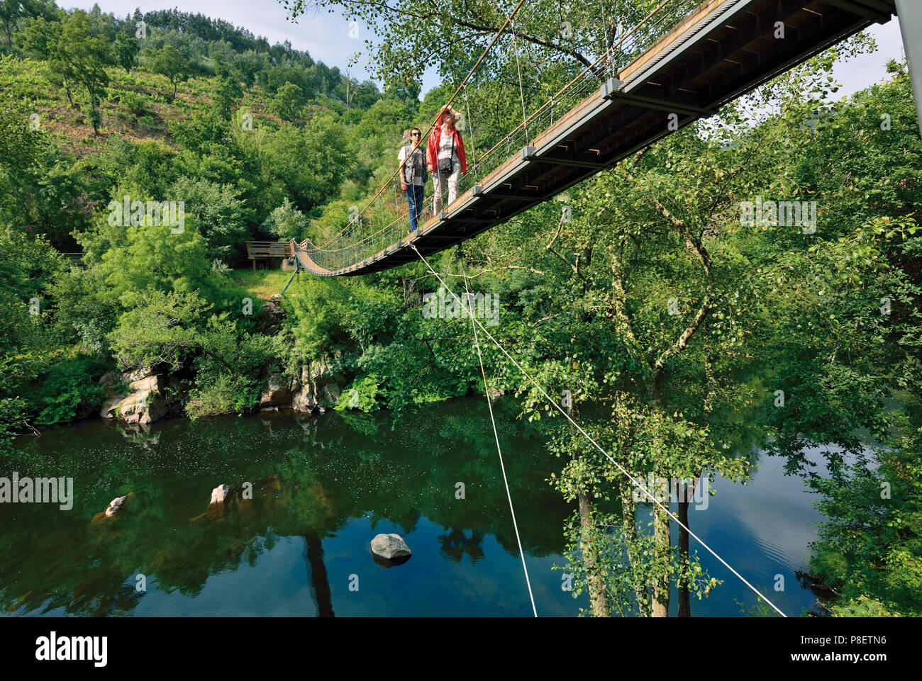 Woman and man crossing suspension bridge over river Stock Photo