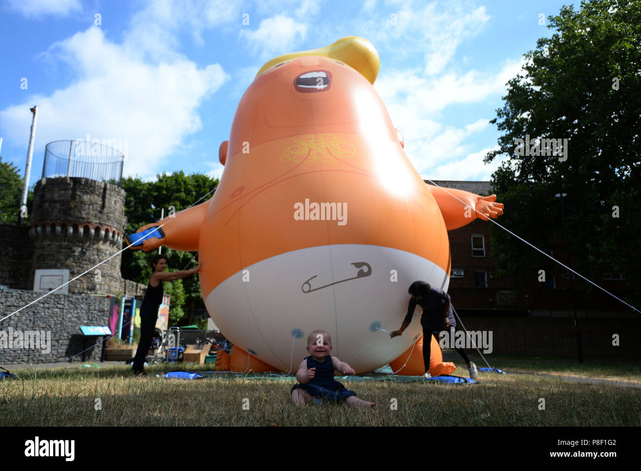 Nine-month-old Ivy Eakin sits in front of the Trump Baby Blimp as is inflated for a practice test, at Bingfield Park in north London. Stock Photo