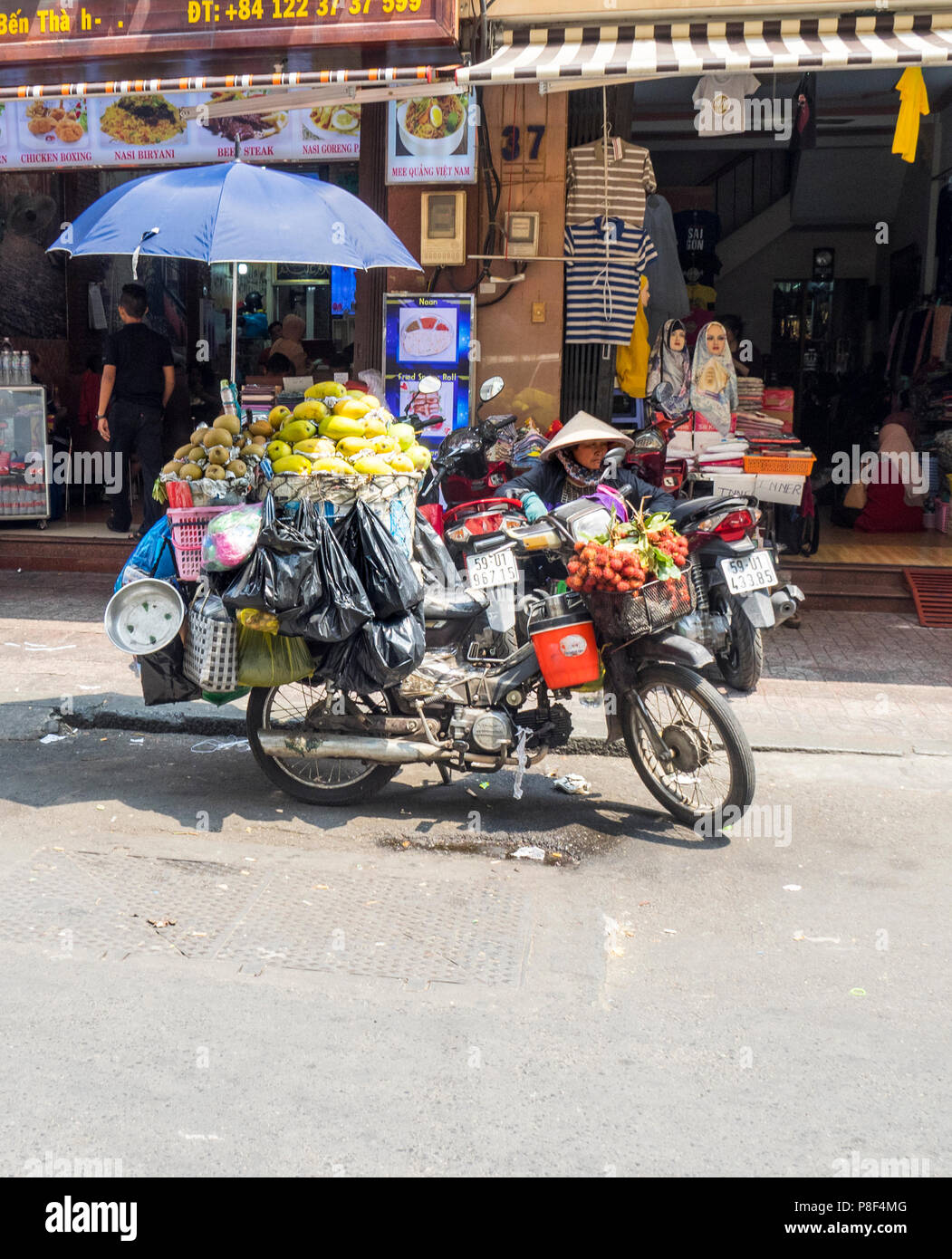 Daily life, a female street vendor selling fruit from her motorbike motorcycle on the street in Ho Chi Minh City, Vietnam. Stock Photo