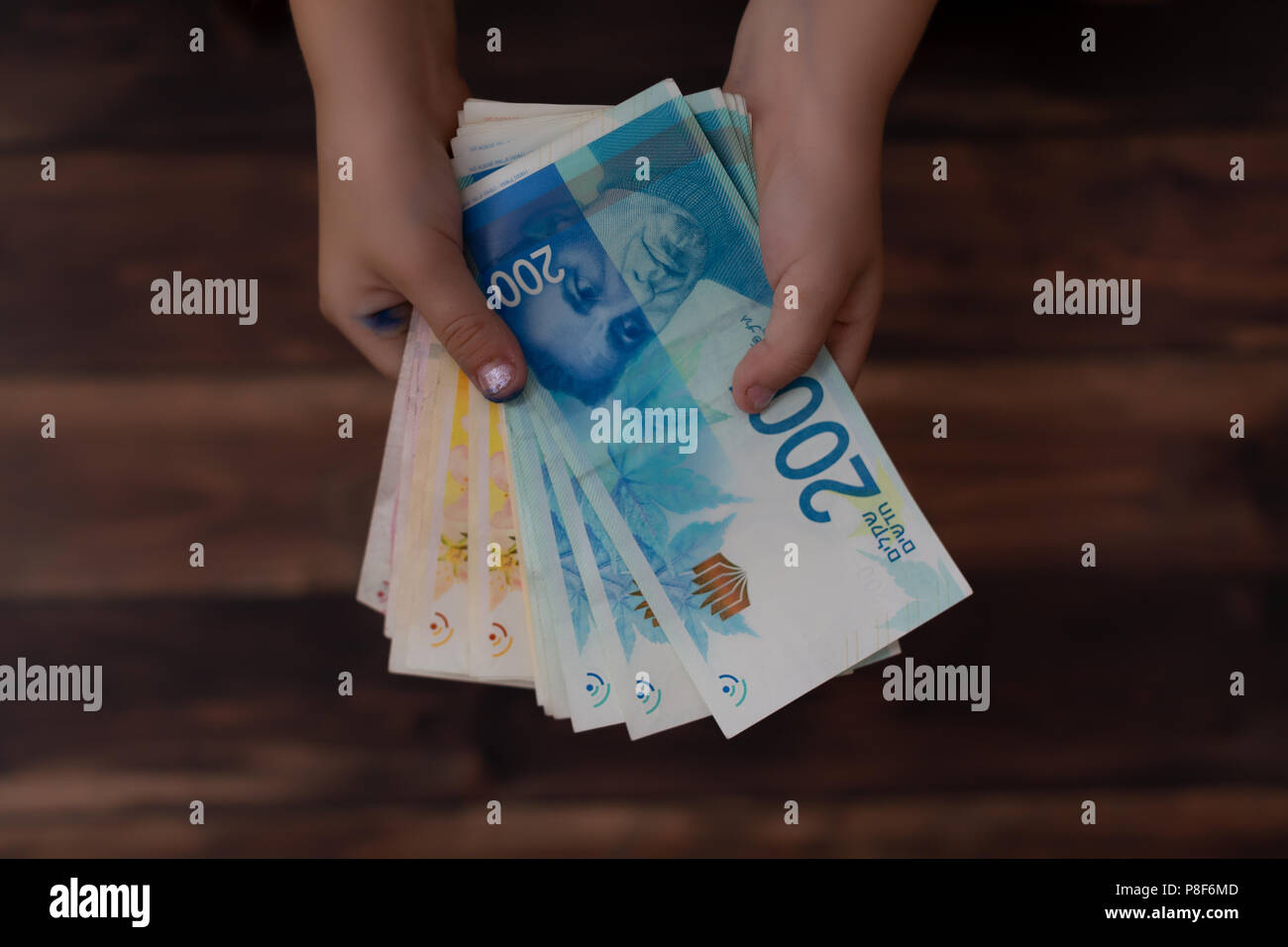 concept of paying money, two hands of children holding Israeli banknotes in 200 shekels ILS Stock Photo
