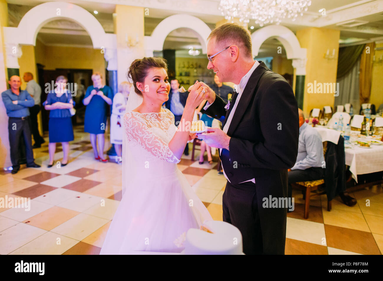 Cheerful newlywed couple is feeding each other with the wedding cake ...