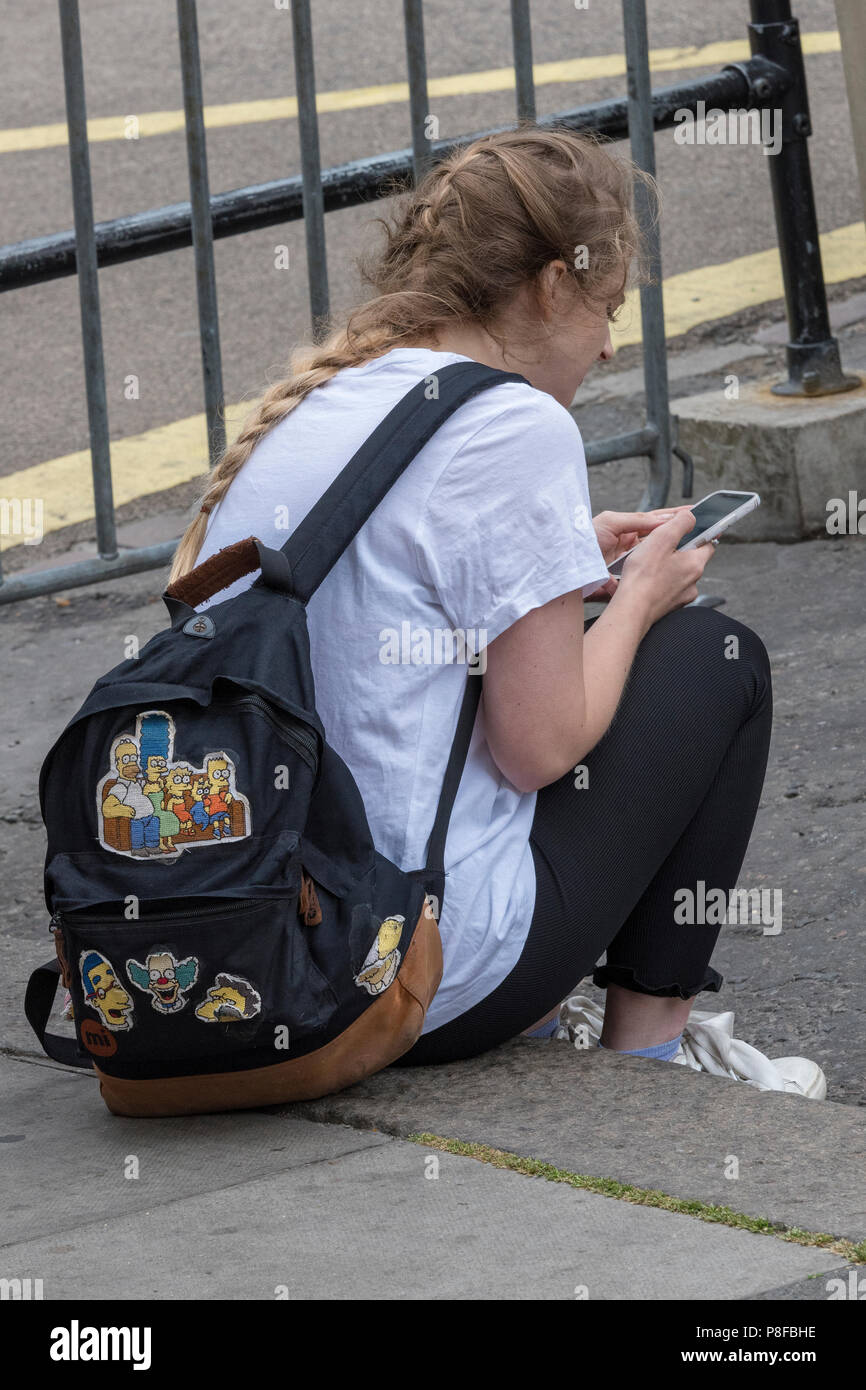 young girl sitting at the side of the road using a smartphone. Stock Photo