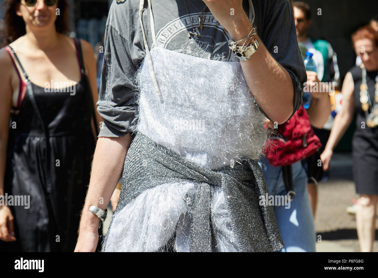 MILAN - JUNE 16: Man with silver shiny dress and skull bracelet before Marni fashion show, Milan Fashion Week street style on June 16, 2018 in Milan. Stock Photo