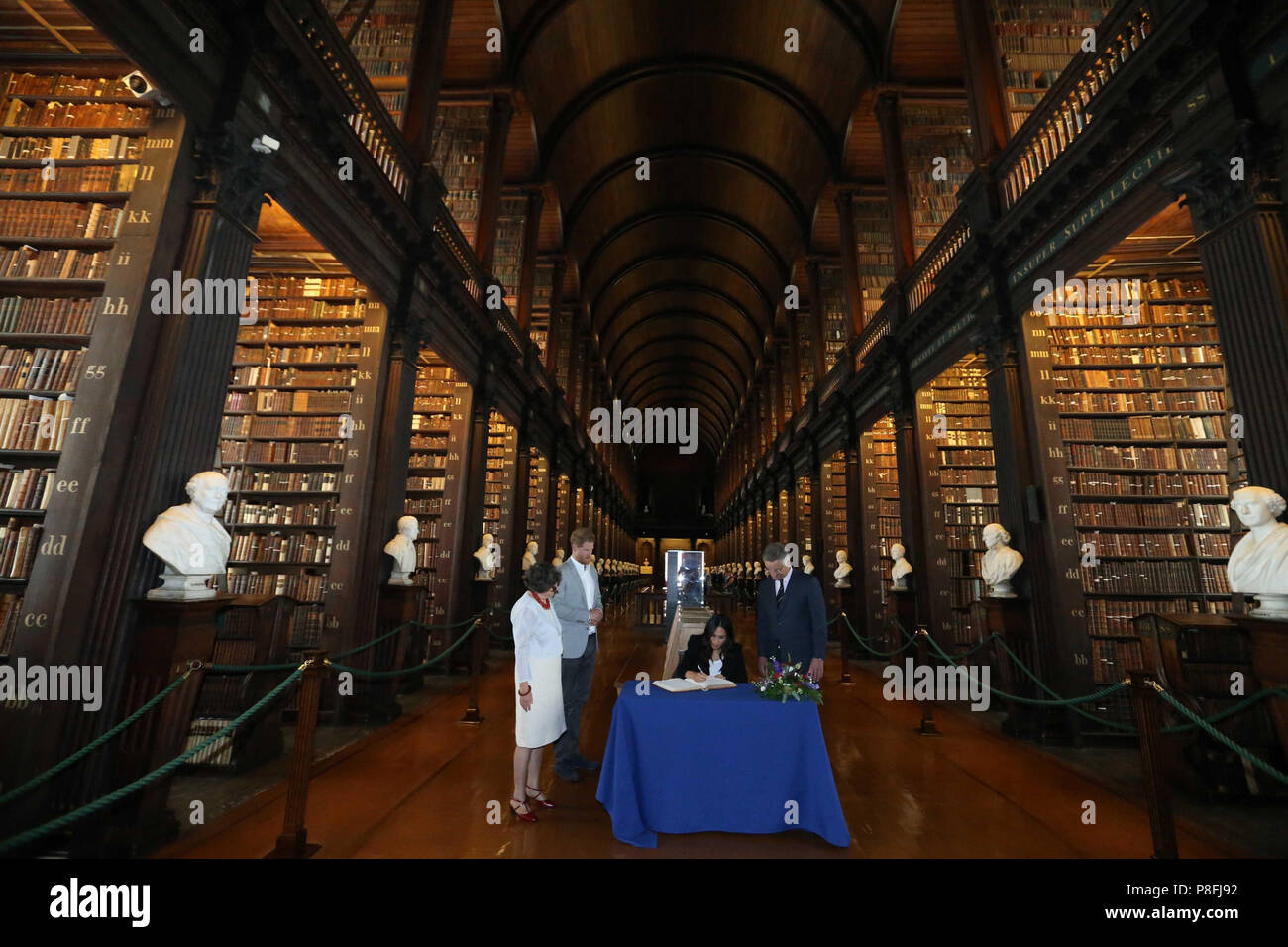 The Duke and Duchess of Sussex sign the visitors book, watched by Trinity, Provost and President, Dr Patrick Prendergast and College Librarian, Helen Shenton in the Long Room of the Old Library as part of their visit to Trinity College Dublin. Stock Photo