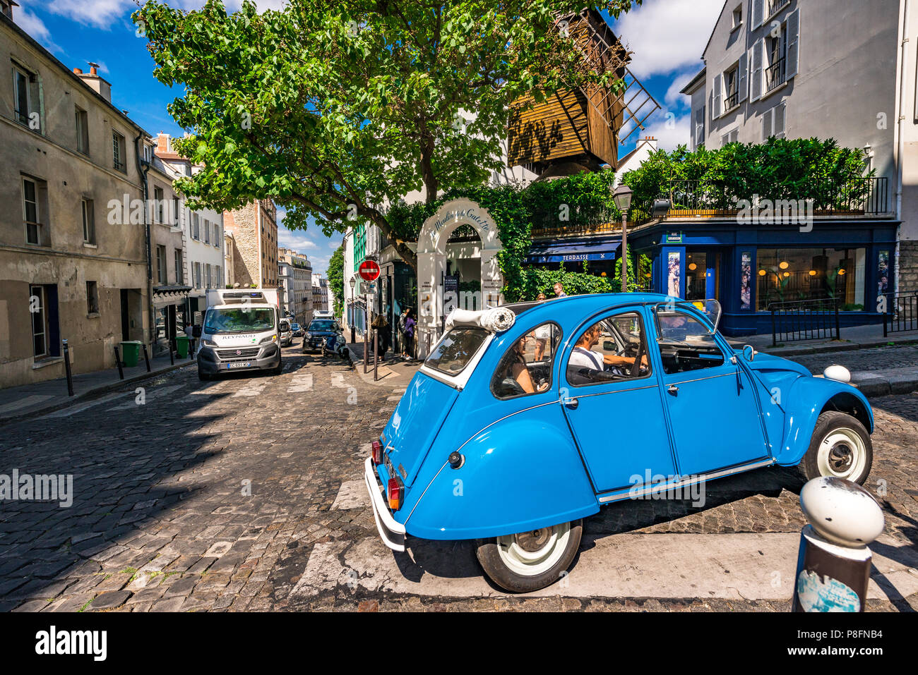 A bright blue Citroen 2CV, 1940's classic car passes the famous Moulin de la Galette in Montmartre, Paris, France Stock Photo