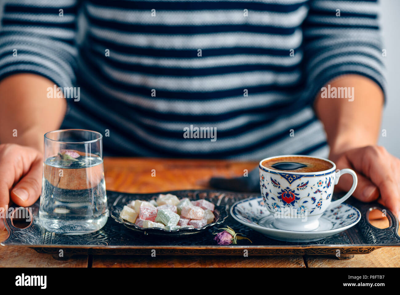 A woman serving Turkish coffee in a traditional Turkish coffee cup on a traditional copper tray