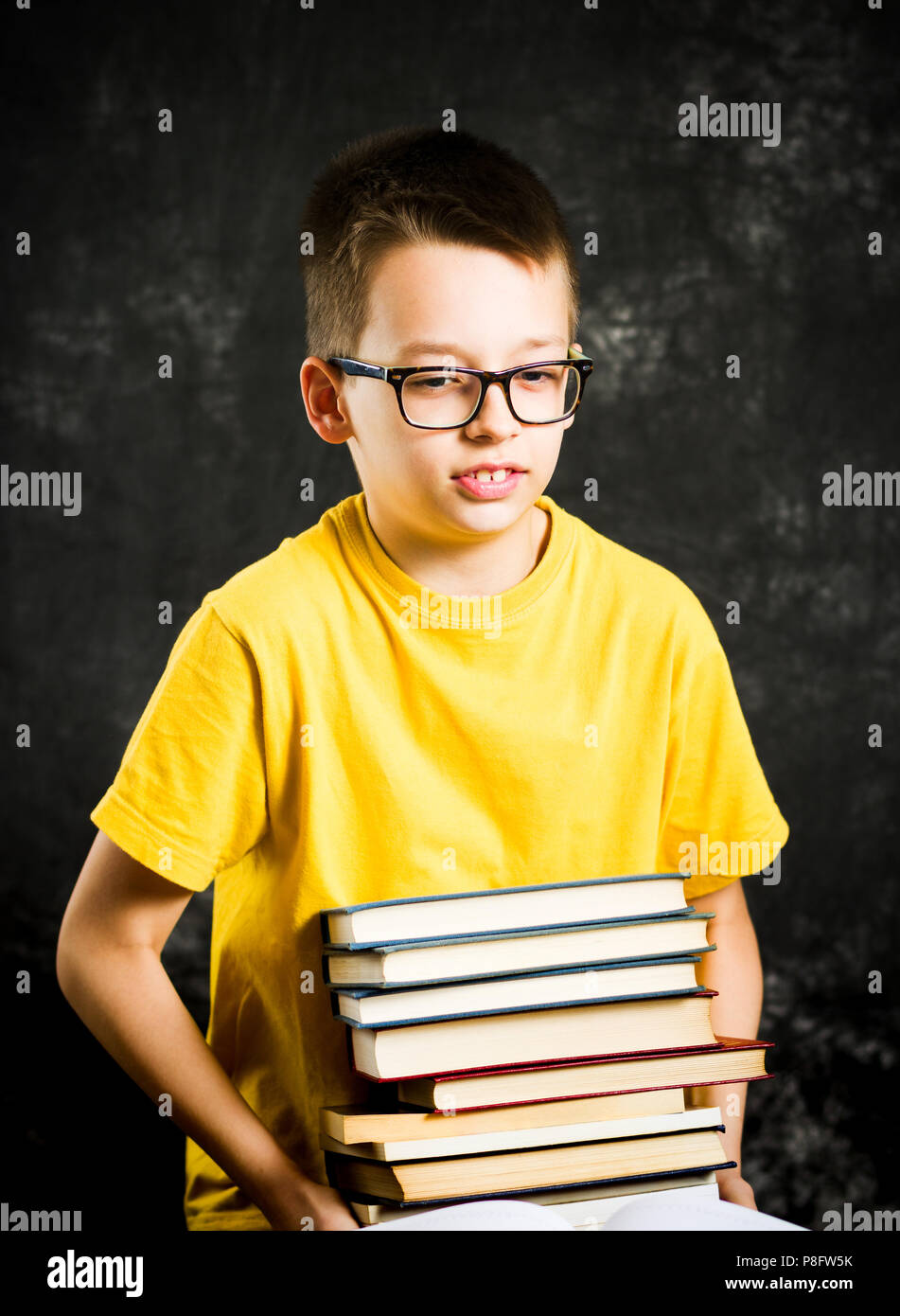 Schoolboy lifting a big and heavy pile of books Stock Photo