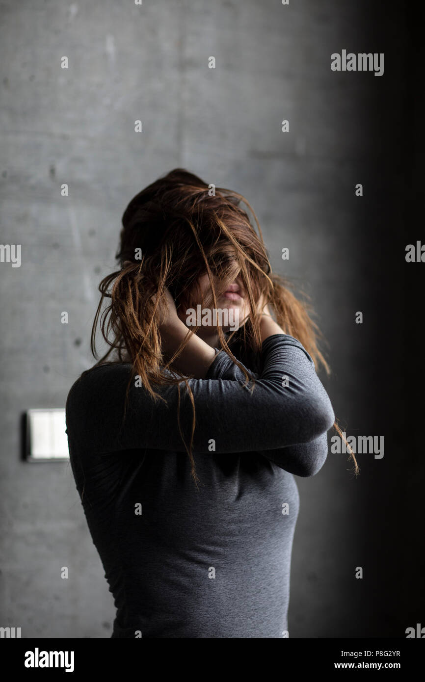 Female Model Posing Behind A Grey Concrete Wall Obscuring Her Face With Own Hair Medium Shot