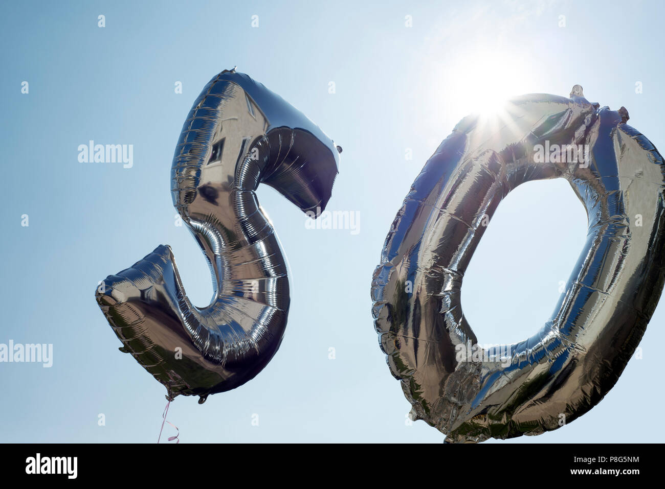 silver balloons for a 50th anniversary floating among the clouds Stock Photo