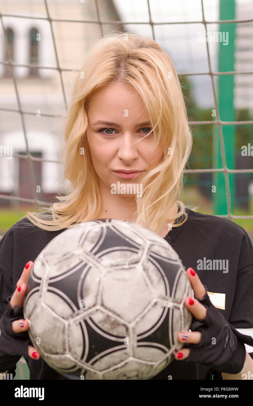 Beautiful blonde with a ball at the football goal. Football field at the gate close-up. Stock Photo