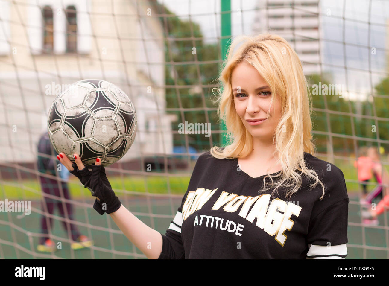 Beautiful blonde with a ball at the football goal. Football field at the gate close-up. Stock Photo