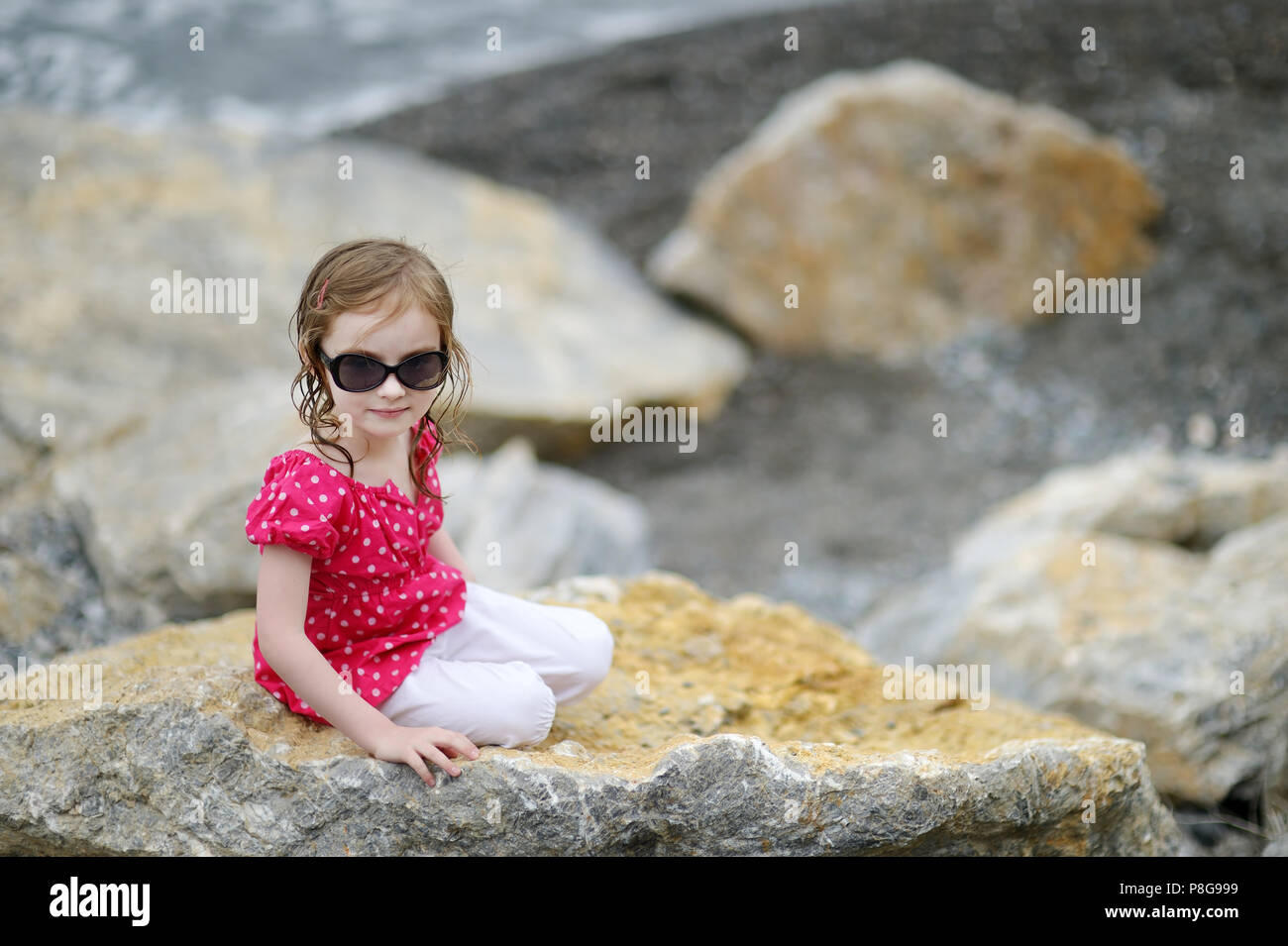 Adorable little girl sitting on a rock by a sea Stock Photo - Alamy