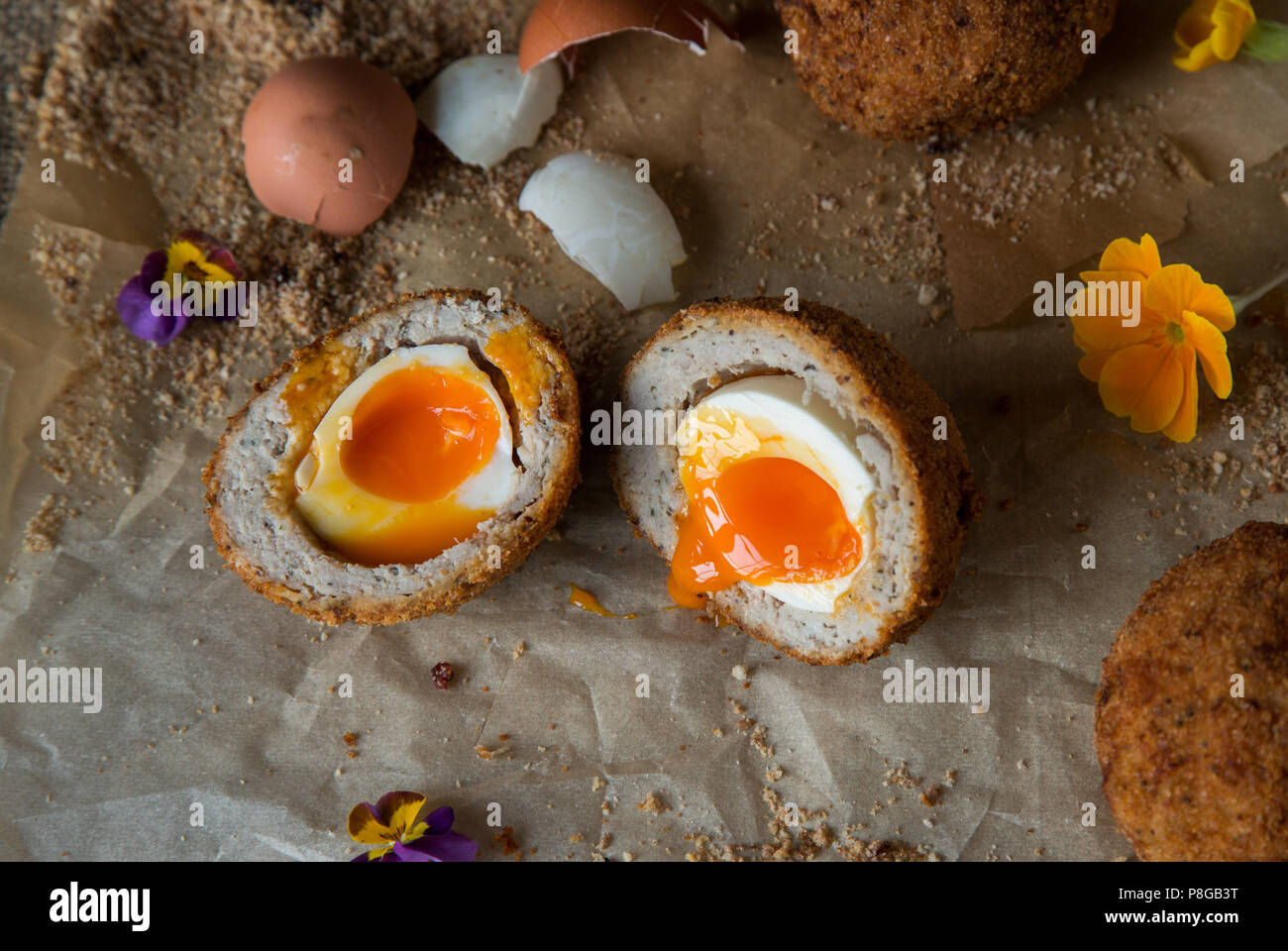 Scotch egg cut open with egg yolk oozing out on parchment paper ...