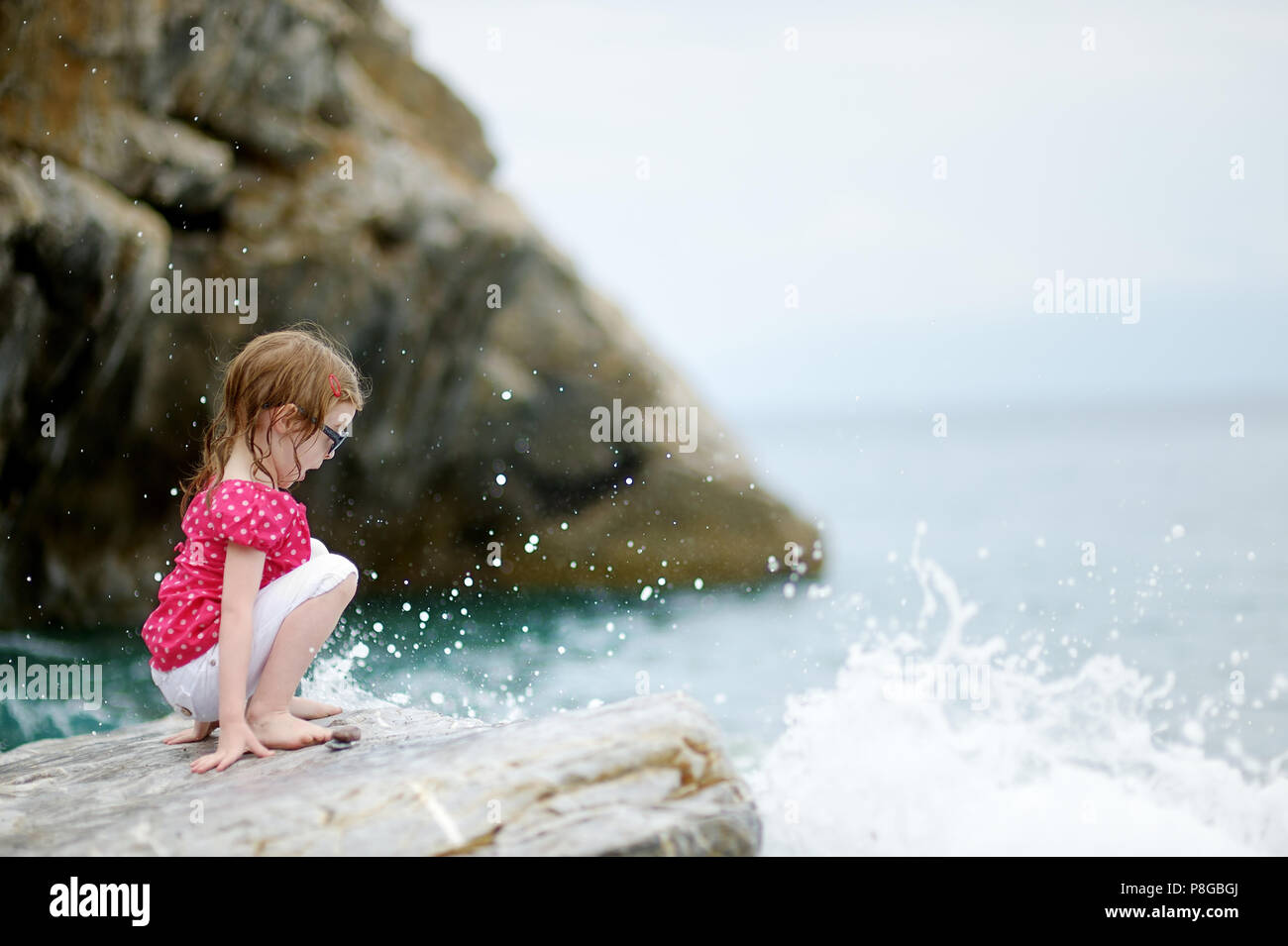 Adorable little girl sitting on a rock by a sea Stock Photo - Alamy