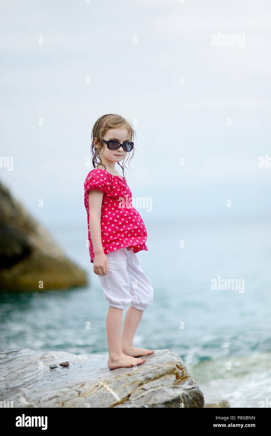 Adorable little girl standing on a rock by a sea Stock Photo - Alamy