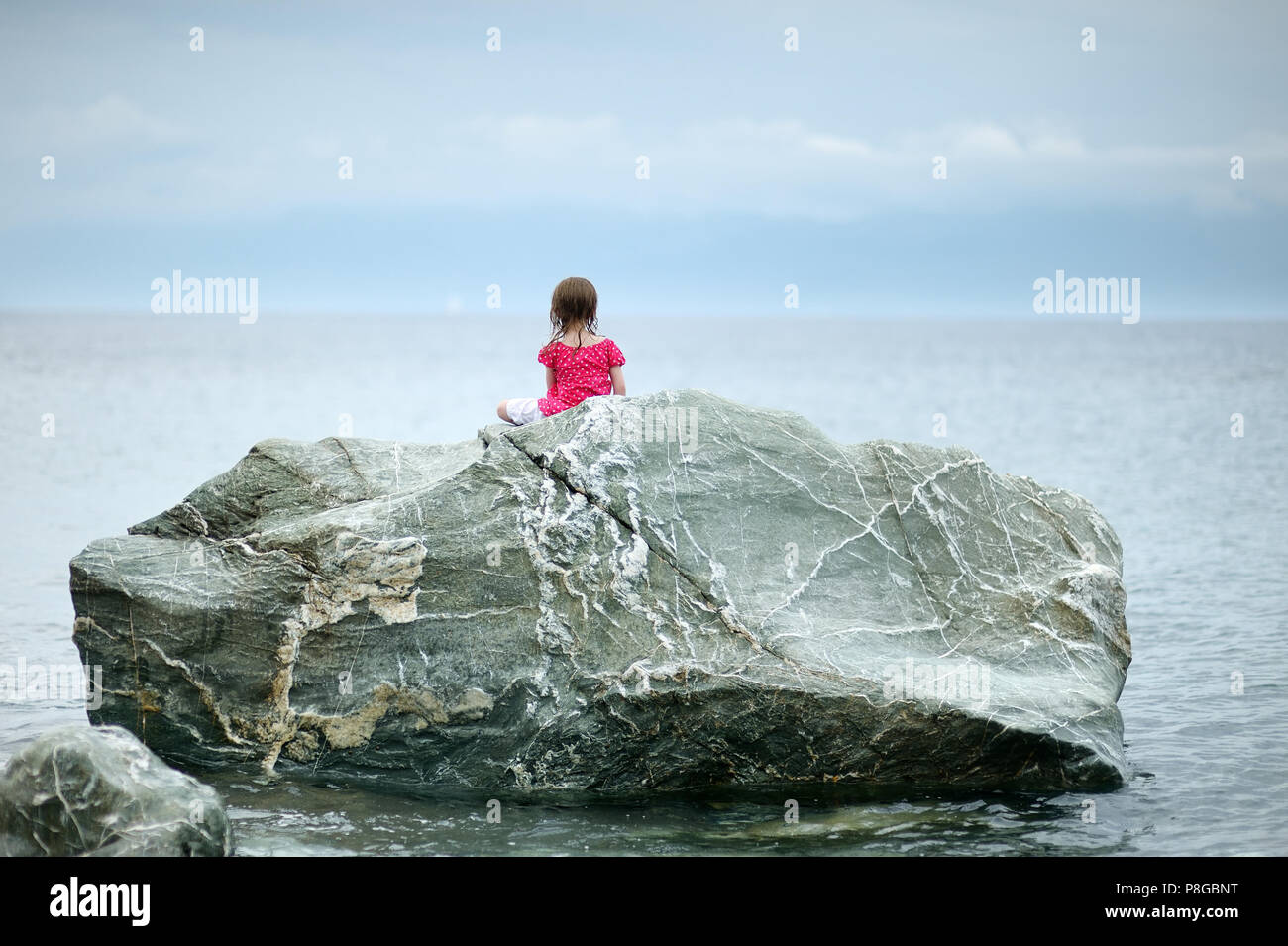 Adorable little girl sitting on a rock by a sea Stock Photo - Alamy