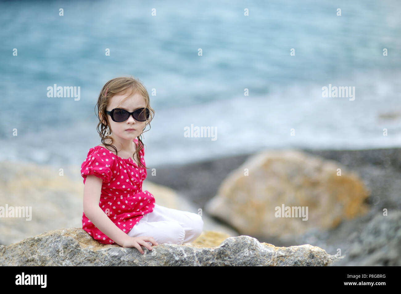 Adorable little girl sitting on a rock by a sea Stock Photo - Alamy