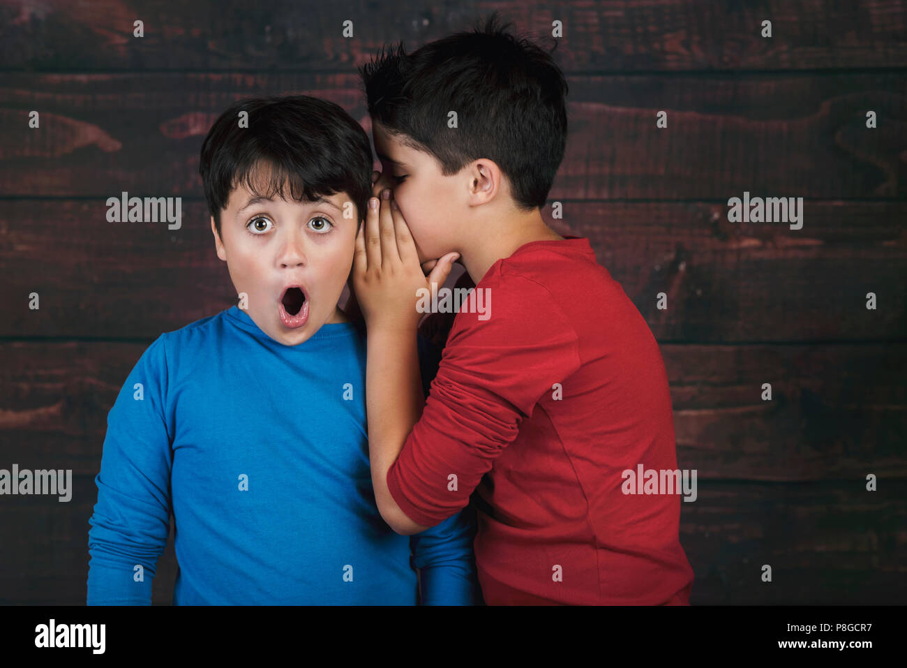 Portrait of two boys whispering secret on wooden background Stock Photo