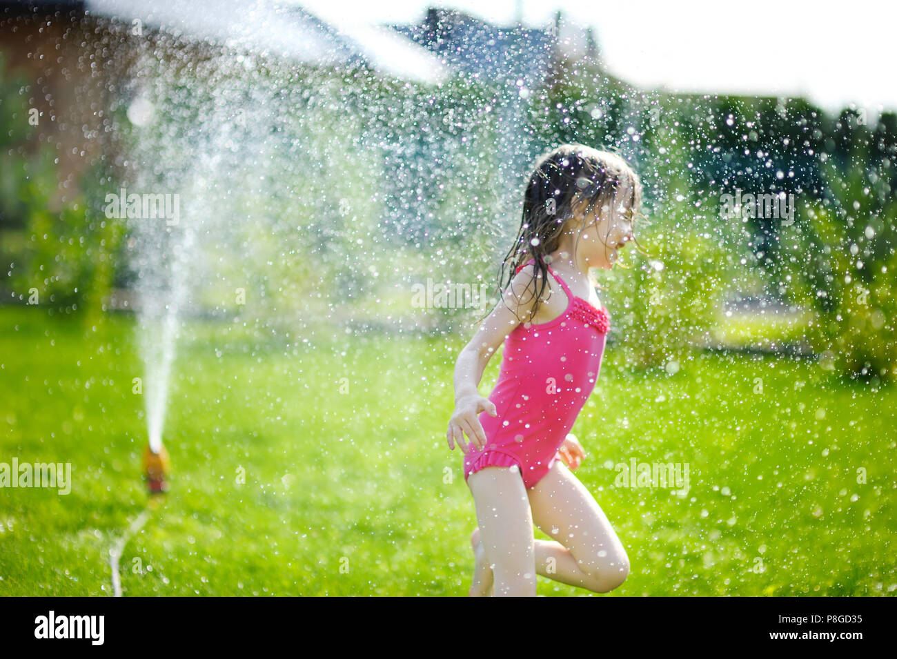 Girl running though a sprinkler in a backyard Stock Photo Alamy