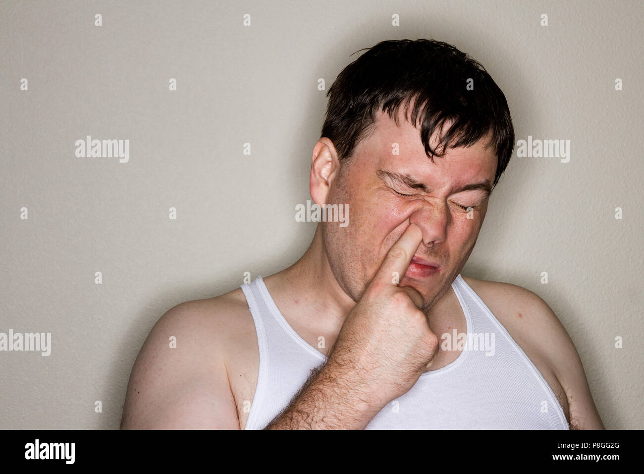 Man being lit with a ring flash standing up against a wall trying to be disgusting an pick a booger out of his nose Stock Photo