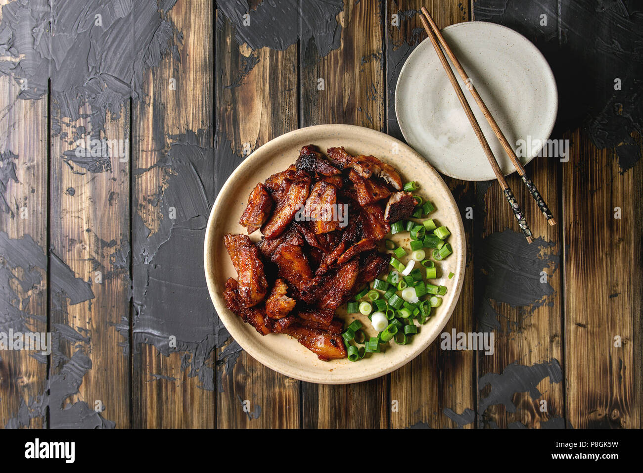 Chinese traditional dish Cantonese BBQ Pork Belly with spring onion served in ceramic plate with chopsticks over dark wooden plank background. Flat la Stock Photo