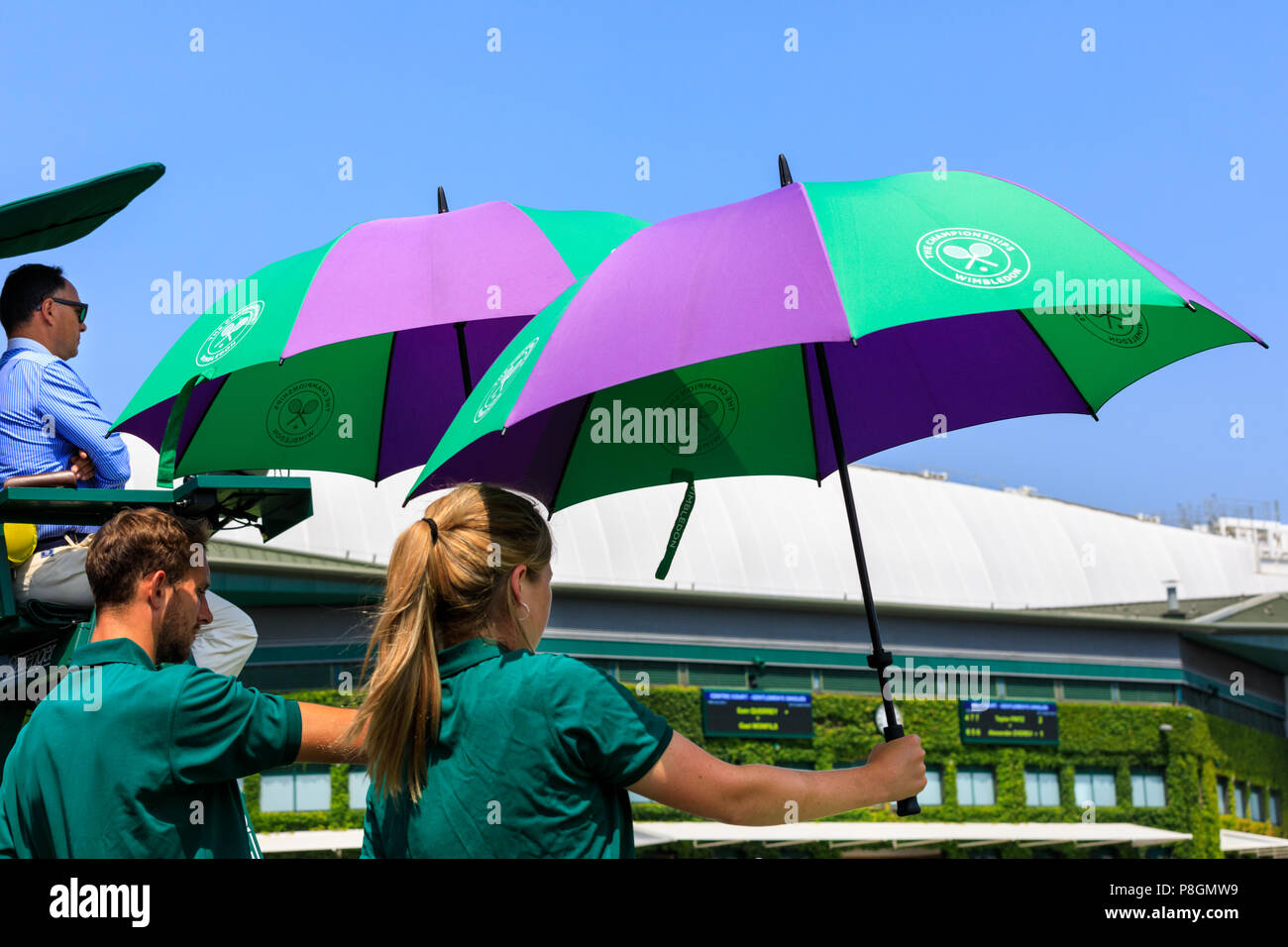 Wimbledon court attendants holding umbrellas above players for shade, All England Lawn Tennis Club Wimbledon, UK Stock Photo